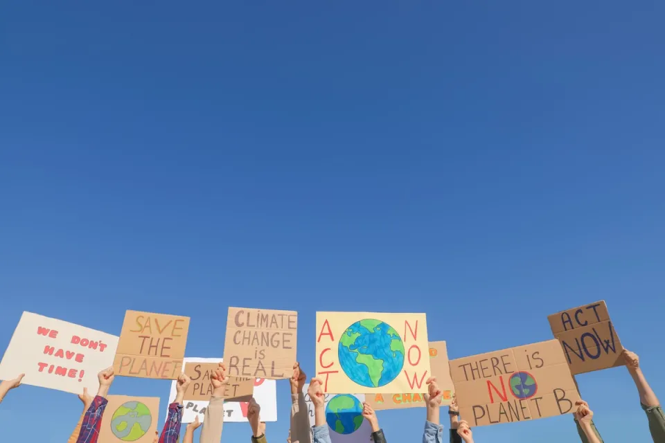 Hands holding up climate change protest signs against blue sky.